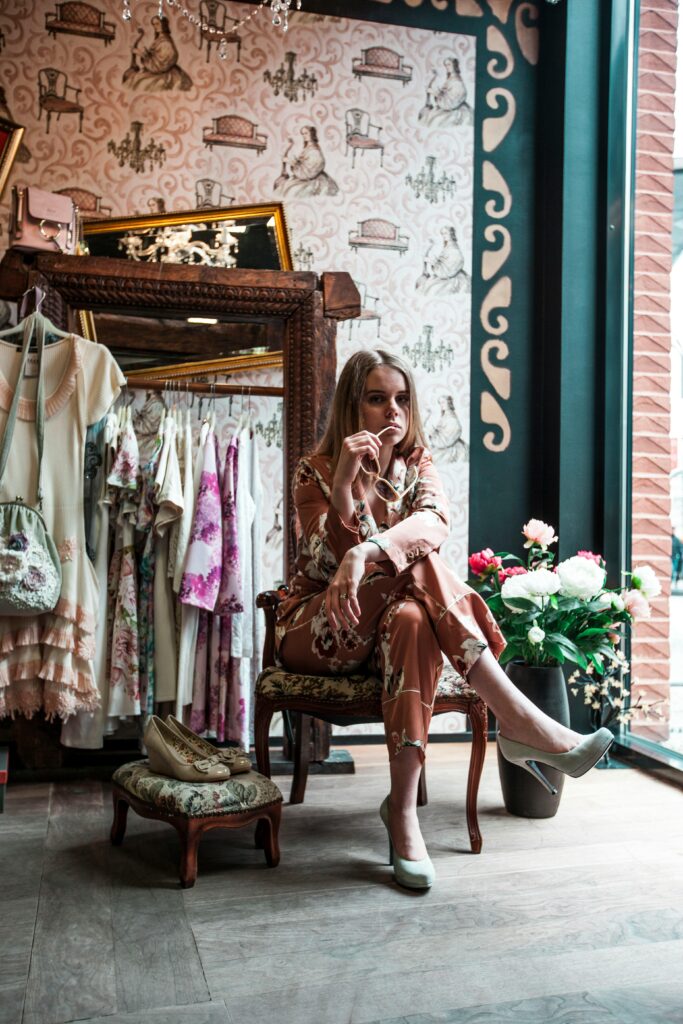 Fashionable woman in a boutique, surrounded by elegant dresses and stylish decor, sitting and posing.